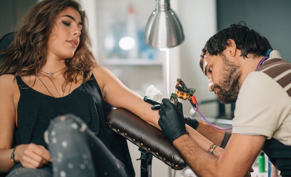 man tattooing woman's arm