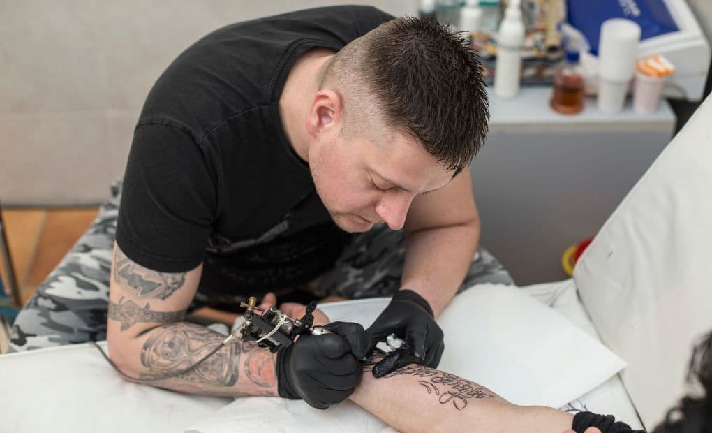 man tattooing arm